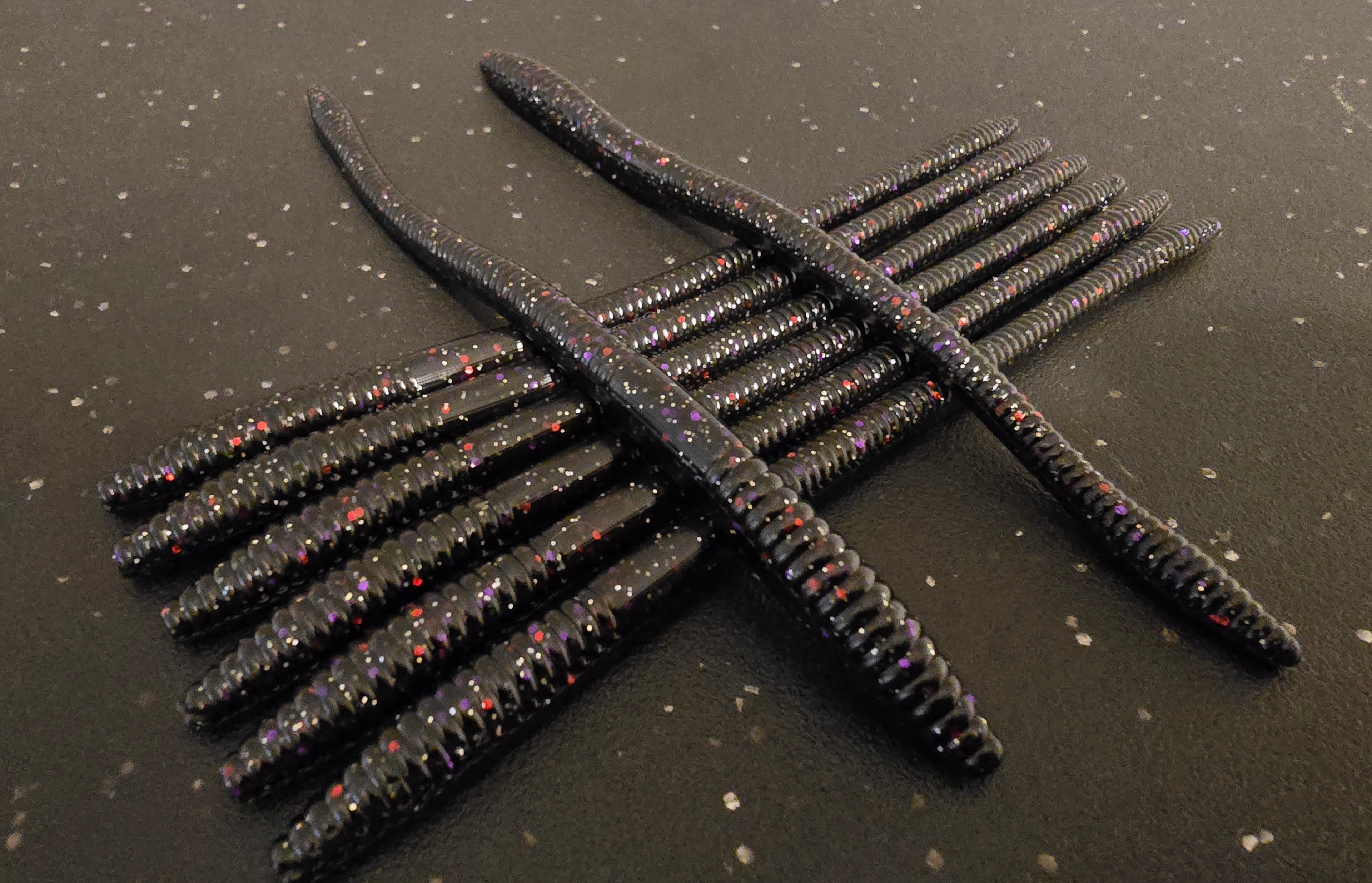 Black fishing lures with red specks arranged in a cross pattern on a dark surface.