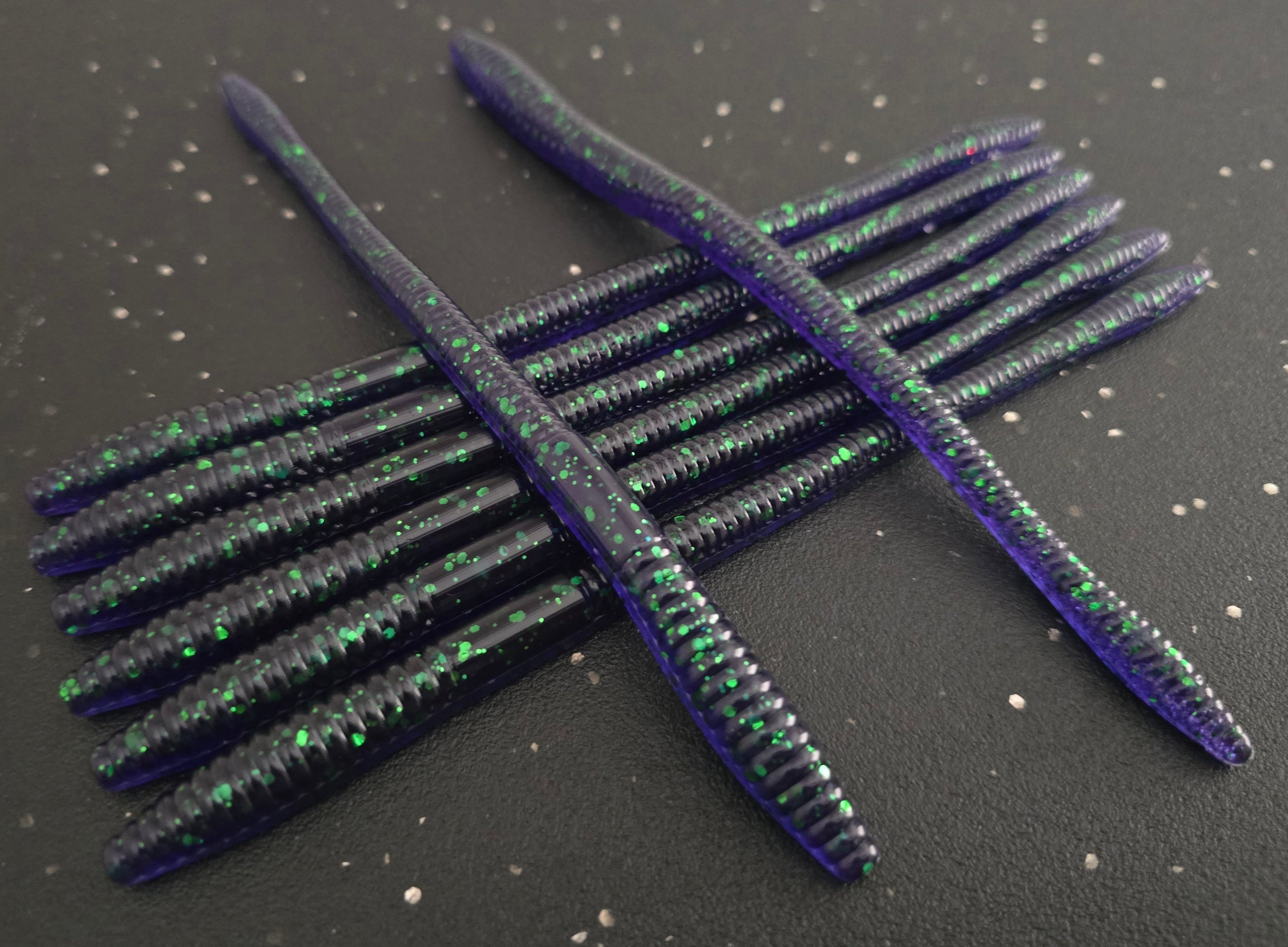 Eight Junebug and green flake Infiltrator worms fishing lures on a dark surface