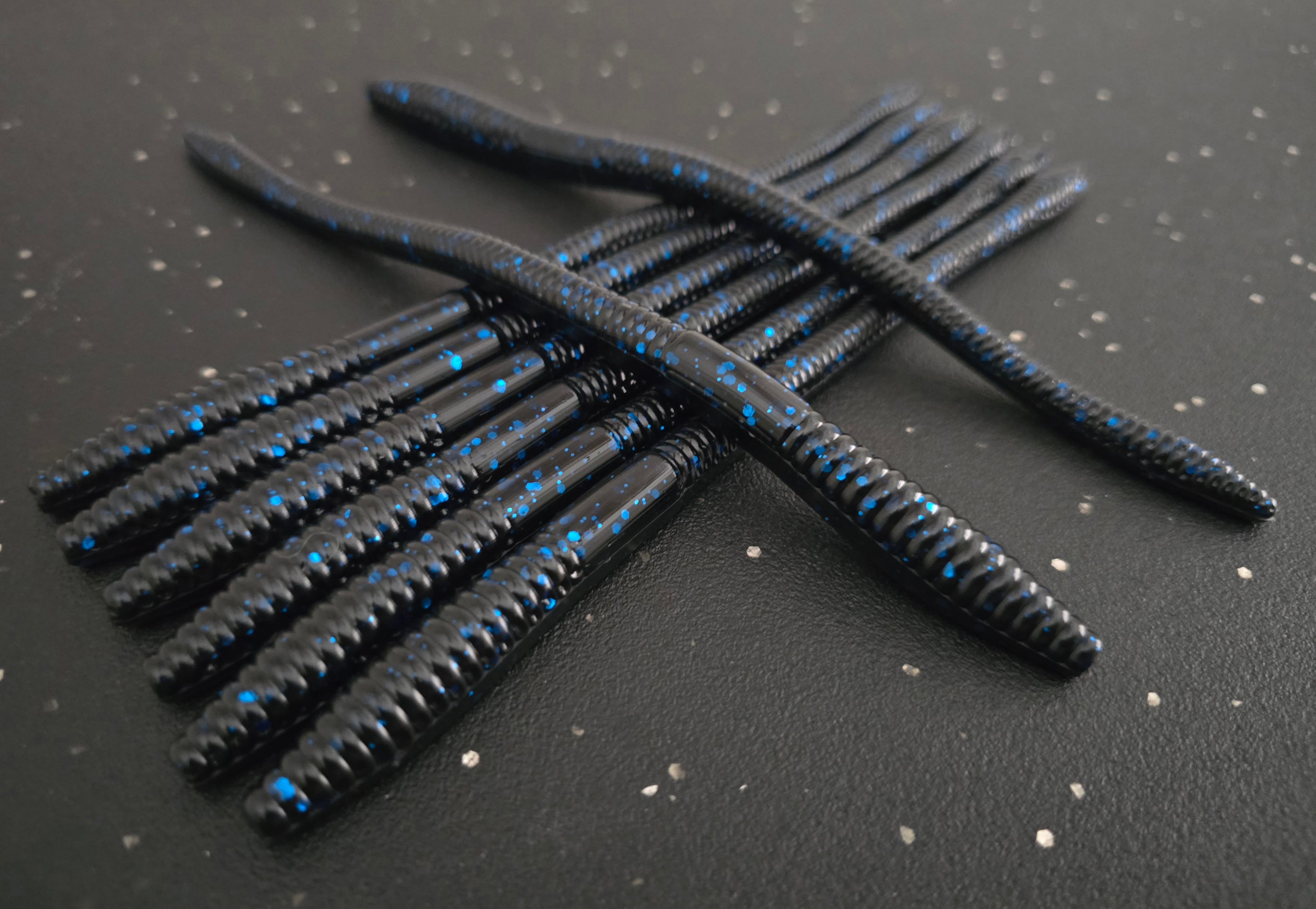 Black infiltrator worm fishing lures with blue flake on a dark surface