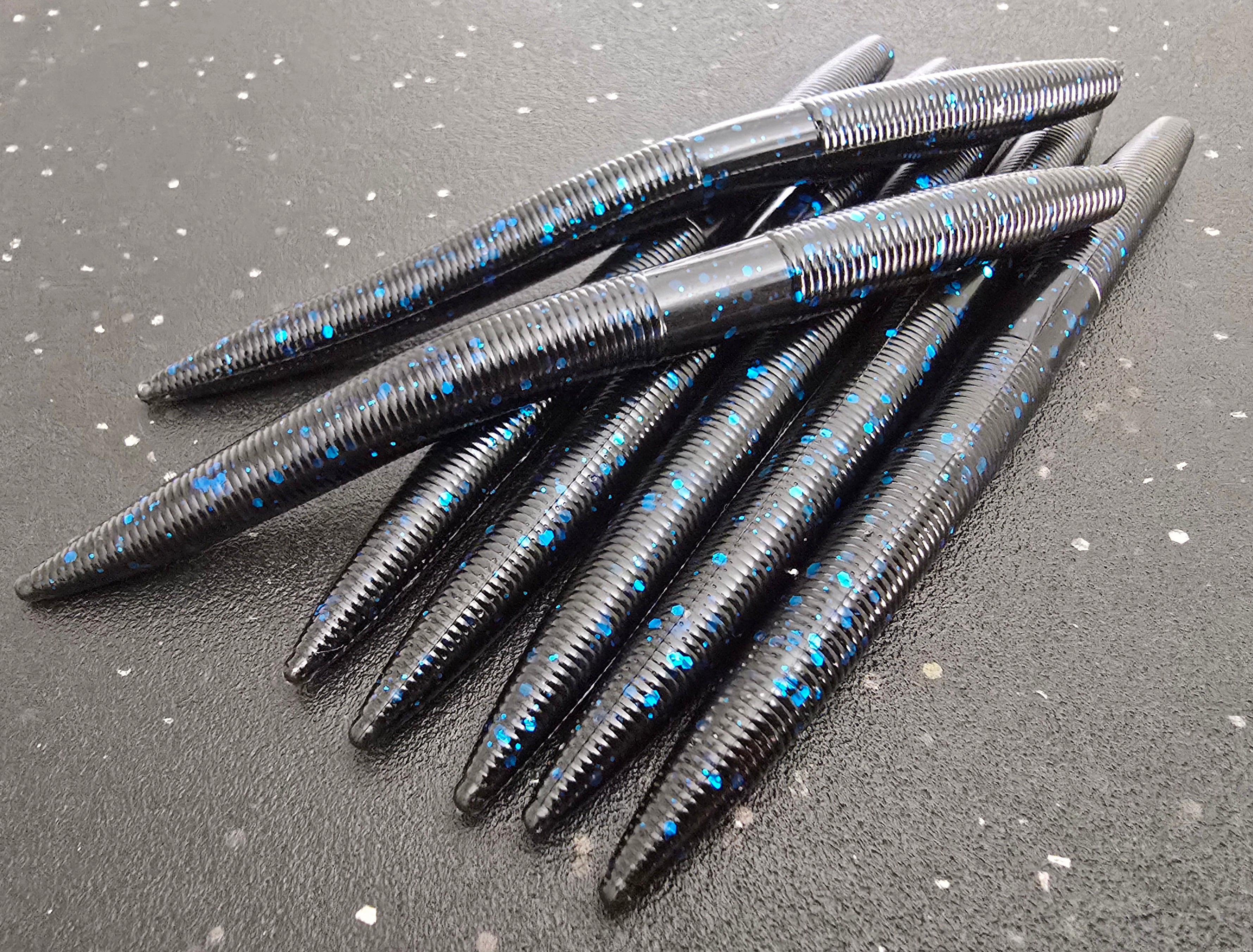 Black and blue sapper sticks soft plastic worms on a gray surface